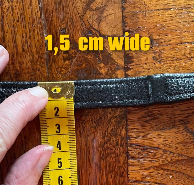 May include: Close-up of a black leather strap measured with a yellow tape measure. The tape measure reads 1.5 cm wide.