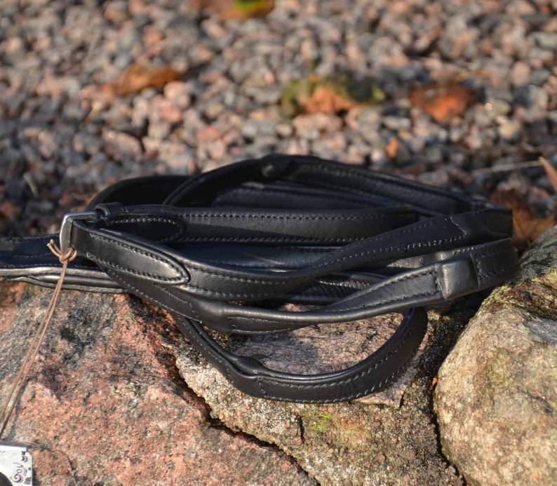 May include: A black leather horse riding bridle folded on a rocky surface. The bridle is made of high-quality leather and has a simple design.