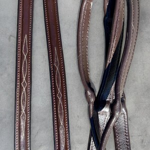 May include: Two sets of brown leather reins with white stitching. One set has a diamond pattern and the other set is plain.