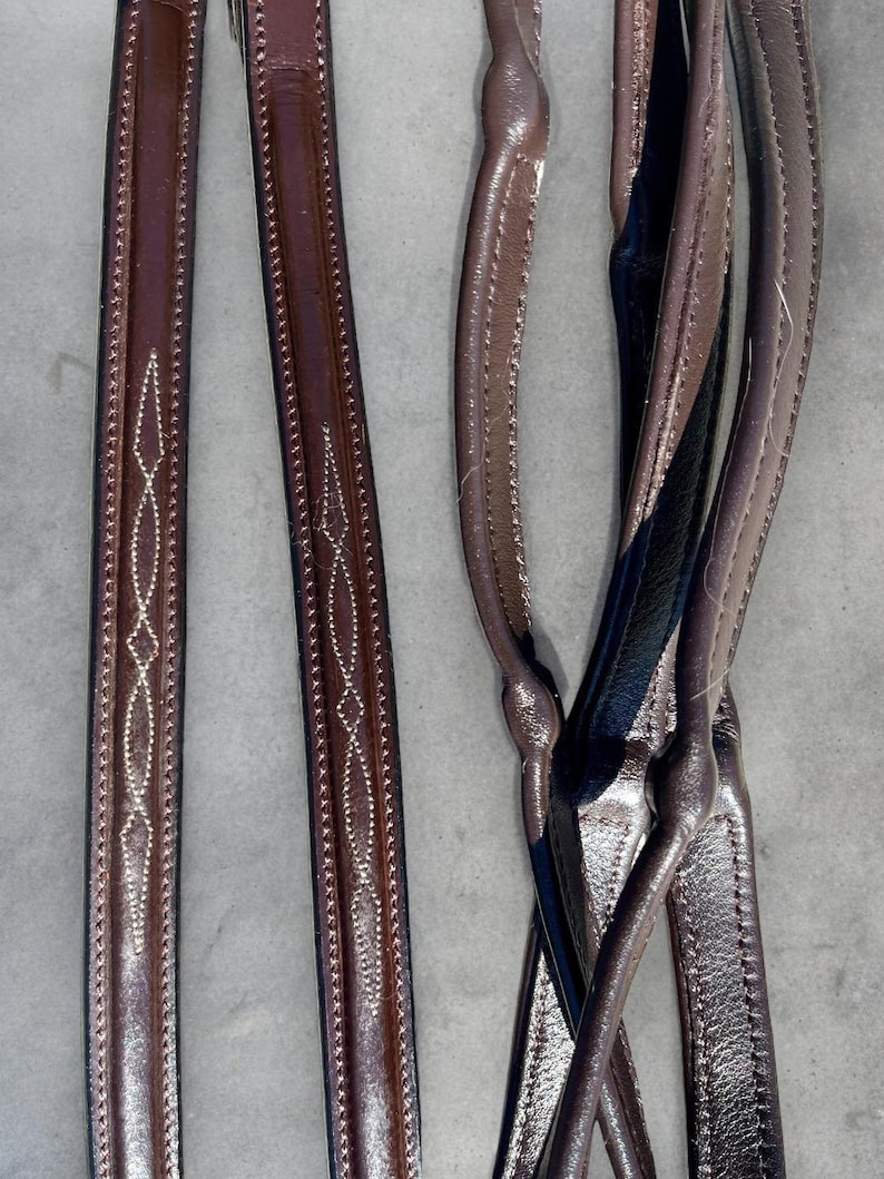 May include: Two sets of brown leather reins with white stitching. One set has a diamond pattern and the other set is plain.