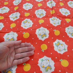 Puede incluir: Tela roja con un patr&oacute;n blanco repetido de un personaje de dibujos animados con una fruta amarilla. La tela tiene peque&ntilde;os puntos blancos.