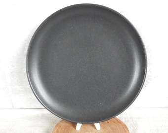 May include: A large, round, black ceramic plate with a slightly textured surface.