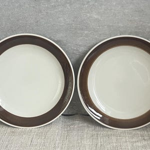 Puede incluir: Dos platos de cerámica blanca con un borde marrón texturizado. Los platos tienen un diseño sencillo y limpio, adecuado para el uso diario o ocasiones especiales. El borde marrón añade un toque de calidez y contraste.