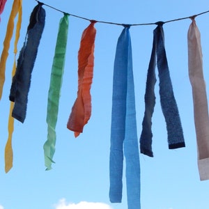 May include: A colorful fabric banner with strips of red, orange, yellow, green, blue, and white hanging against a blue sky.