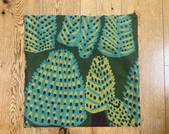 May include: A green fabric cushion cover with a repeating pattern of stylized trees in shades of green, blue, and yellow.