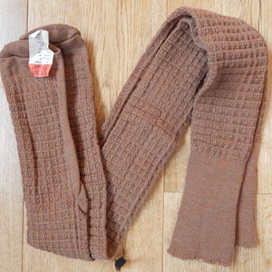 Puede incluir: Un par de polainas de punto marrón con textura acanalada. Las polainas están dobladas por la mitad y tienen una etiqueta adjunta.