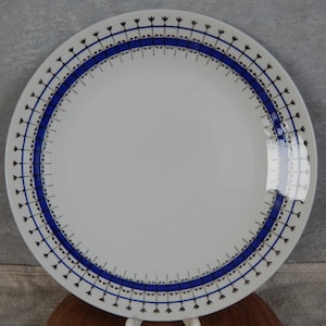 May include: White ceramic dinner plate with a blue and black border design. The border features a repeating pattern of small black flowers and a blue band.