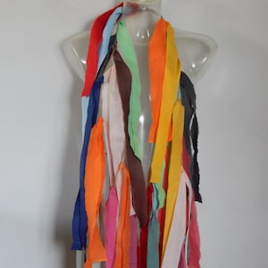 May include: A colorful scarf made of fabric strips in various colors, including red, orange, yellow, green, blue, and pink. The scarf is displayed on a mannequin.