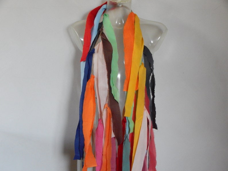 May include: A colorful scarf made of fabric strips in various colors, including red, orange, yellow, green, blue, and pink. The scarf is displayed on a mannequin.