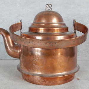 Könnte beinhalten: Ein Kupferkessel mit einem gewölbten Deckel und einem Griff. Der Kessel hat ein abgenutztes, altes Aussehen.