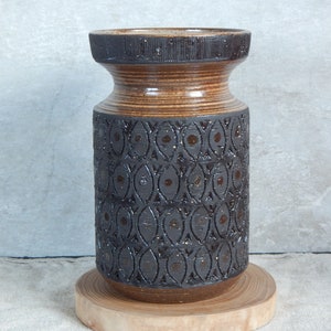 Puede incluir: Un jarrón de cerámica marrón y negro con un patrón geométrico. El jarrón tiene una boca ancha y una base estrecha.