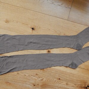 May include: A pair of brown thigh-high stockings laid out flat on a wooden surface.