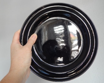 May include: A black ceramic dinner plate with a glossy finish and a slightly raised rim.