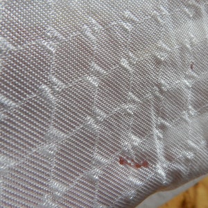 May include: White fabric with a textured, diamond-shaped pattern. The fabric has a subtle sheen and a slightly rough texture.