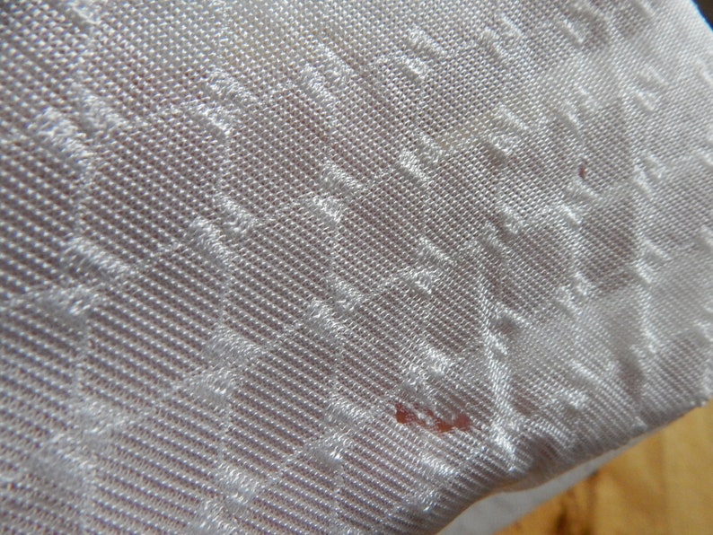 May include: White fabric with a textured, diamond-shaped pattern. The fabric has a subtle sheen and a slightly rough texture.