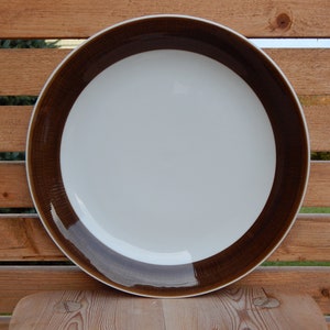 May include: A white ceramic dinner plate with a brown rim. The rim has a textured pattern.