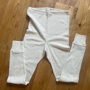 May include: White thermal underwear long johns with a ribbed texture. The underwear has a high waist and a fitted leg.