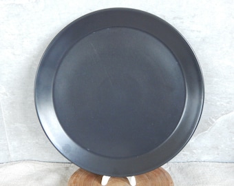 May include: A large, round, black ceramic plate with a slightly raised rim.
