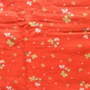 Puede incluir: Tela roja con un patr&oacute;n floral blanco y verde. La tela tiene una superficie texturizada.