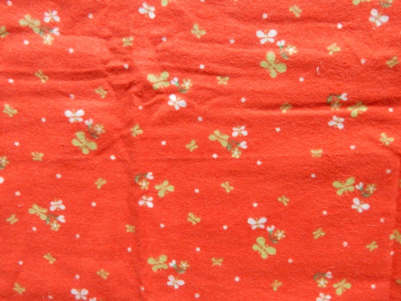 Puede incluir: Tela roja con un patr&oacute;n floral blanco y verde. La tela tiene una superficie texturizada.