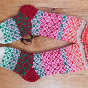 May include: A pair of knitted socks with a colorful geometric pattern in shades of red, pink, green, and white.