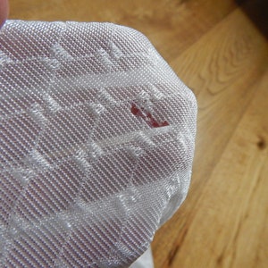 May include: Close-up of a white, textured fabric with a small red stain.