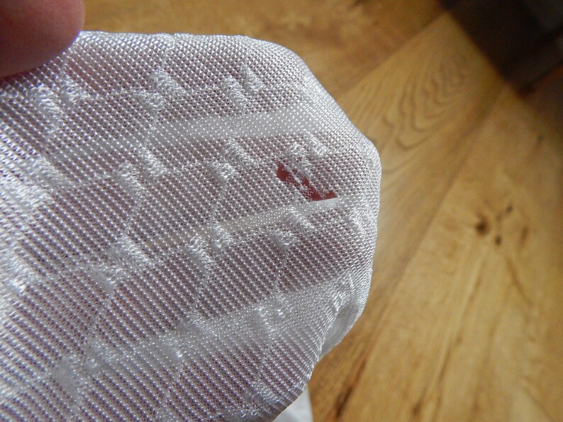 May include: Close-up of a white, textured fabric with a small red stain.