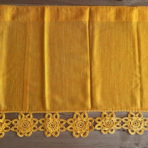 Op de afbeelding: Een goudgele tafelloper met een geweven textuur en een decoratieve gehaakte bloemenrand. De loper is gemaakt van een geweven materiaal en is geschikt voor een eettafel of andere oppervlakken.
