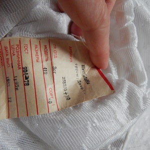 May include: A white tag with black text and red lines. The tag has information about the product, including the model number, size, and price. The text on the tag reads: "ARTIKUL TRUSY DEV", "255380+30", "GR. OT", "35", "MODEL 412", "COPT 40", "RAZMER", "GOST 904 78", "ROZNI4NAYA", "TSENA 1.95K", "DATA VYP 1983", "12", "PROCHNAYA".