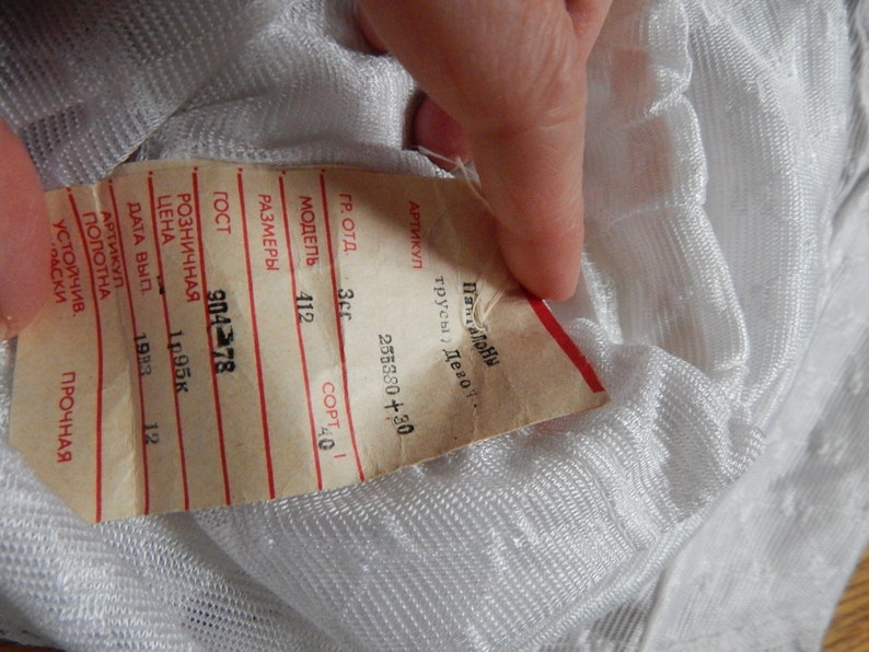 May include: A white tag with black text and red lines. The tag has information about the product, including the model number, size, and price. The text on the tag reads: "ARTIKUL TRUSY DEV", "255380+30", "GR. OT", "35", "MODEL 412", "COPT 40", "RAZMER", "GOST 904 78", "ROZNI4NAYA", "TSENA 1.95K", "DATA VYP 1983", "12", "PROCHNAYA".
