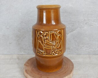 Peut inclure: Un vase en céramique brun avec un motif en relief de trois personnages dans une scène. Le vase a un corps arrondi et un col étroit.
