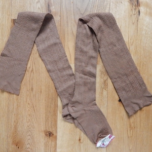 Peut inclure: Une paire de collants côtelés marrons pliés sur une surface en bois.
