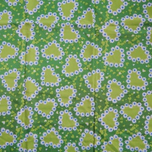 May include: Green fabric with a repeating pattern of lime green hearts outlined with white daisies and blue centers. The background is a darker green with small green hearts scattered throughout.