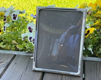 May include: A silver picture frame with an ornate design. The frame is empty and has a reflective surface.