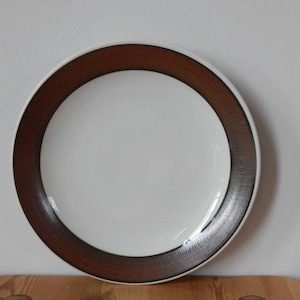 May include: A white ceramic plate with a brown rim. The rim has a textured design.