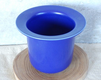 May include: A deep blue ceramic planter with a wide, rounded rim. The planter is sitting on a wooden surface.