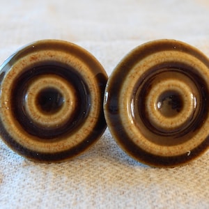 Puede incluir: Dos pomos de cerámica marrón y beige con un diseño de círculos concéntricos.