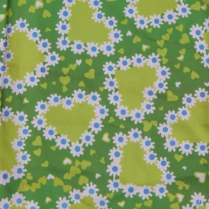 May include: Green fabric with a repeating pattern of lime green hearts outlined with white daisies and blue centers. Small green and white hearts are scattered across the background.