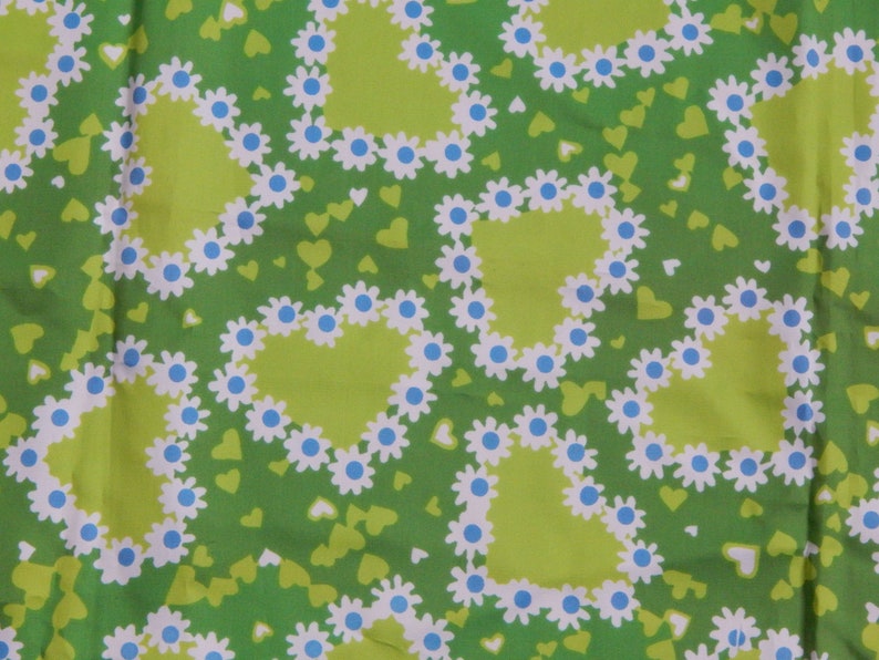 May include: Green fabric with a repeating pattern of lime green hearts outlined with white daisies and blue centers. Small green and white hearts are scattered across the background.