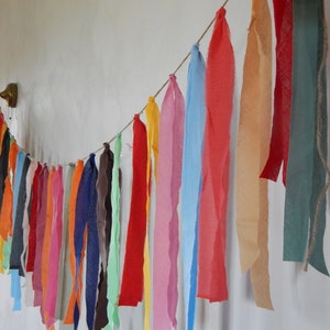 May include: A colorful fabric garland with strips of various colors, including red, orange, yellow, green, blue, and purple, hanging from a string.