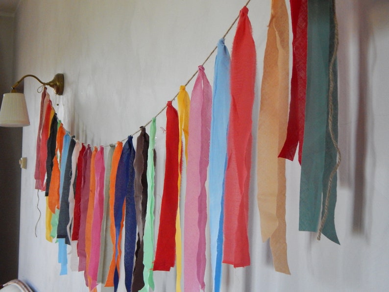May include: A colorful fabric garland with strips of various colors, including red, orange, yellow, green, blue, and purple, hanging from a string.