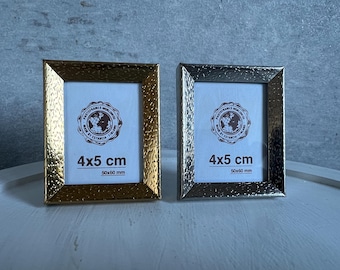 May include: Two 4x5 inch picture frames, one gold and one silver, with a textured finish. Both frames have a label that reads "4x5 cm 50x60 mm".