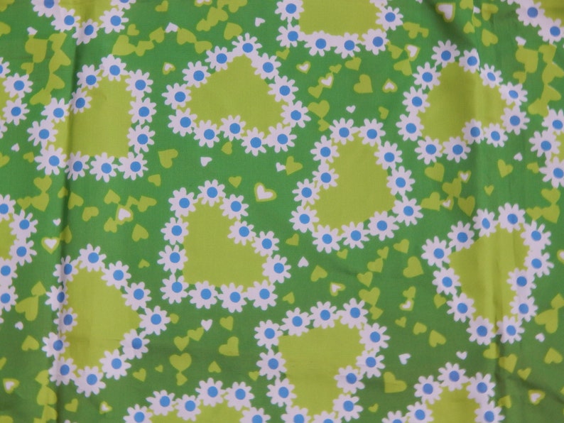 May include: A green fabric with a repeating pattern of lime green hearts outlined with white daisies and blue centers. Small green and white hearts fill the background. The fabric has a retro, floral design.