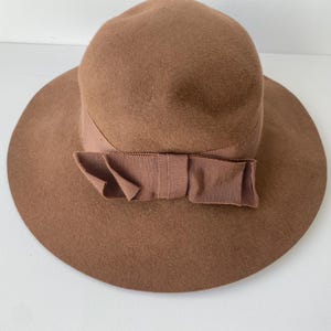Puede incluir: Un sombrero de lana marrón con ala ancha y lazo de cinta a juego. El sombrero tiene un diseño clásico y elegante, adecuado para diversas ocasiones. El ala del sombrero tiene un diámetro de unos 30 cm.