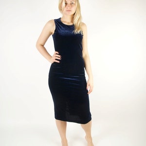 May include: A sleeveless, navy blue velvet dress. The dress is knee-length and form-fitting, with a simple, elegant design. The fabric has a soft, luxurious appearance.