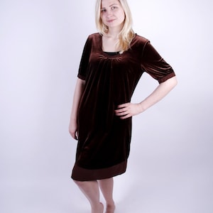 May include: A brown velvet dress with short sleeves and a scoop neckline. The dress has a darker brown trim at the hem and sleeves. The dress is knee-length.