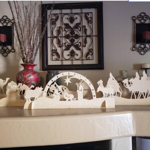 May include: A wooden nativity scene with a star on top, a stable, and figures of Mary, Joseph, and the baby Jesus. There are also figures of three wise men riding camels and a donkey and a cow.