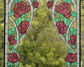 Op de afbeelding: Een glas-in-lood raamontwerp met twee symmetrische panelen met een herhalend patroon van rozen en bladeren. De rozen zijn diep roze van kleur en de bladeren zijn een levendig groen. De panelen zijn geplaatst tegen een achtergrond van een wazige groene boom.