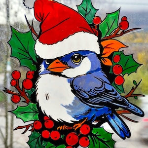 Op de afbeelding: Een feestelijke raamsticker met een blauwe vogel die een rode kerstmuts met witte rand draagt. De vogel is omringd door groene hulstbladeren en heldere rode bessen, wat een kerstthema creëert. Het kunstwerk heeft gedetailleerde zwarte contouren en levendige kleuren.