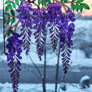Peut inclure: Panneau de fenêtre en vitrail représentant des glycines. Le motif présente des fleurs de glycine violettes suspendues à des branches brunes avec des feuilles vertes. Le panneau est souligné en noir, sur un fond extérieur flou.